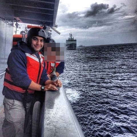 Two men wearing life jackets and helmets outside on the side of a ship in the ocean