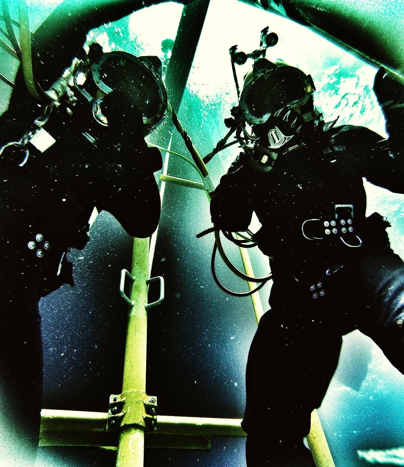 Two divers underwater standing next to each other holding their regulators on their helmets