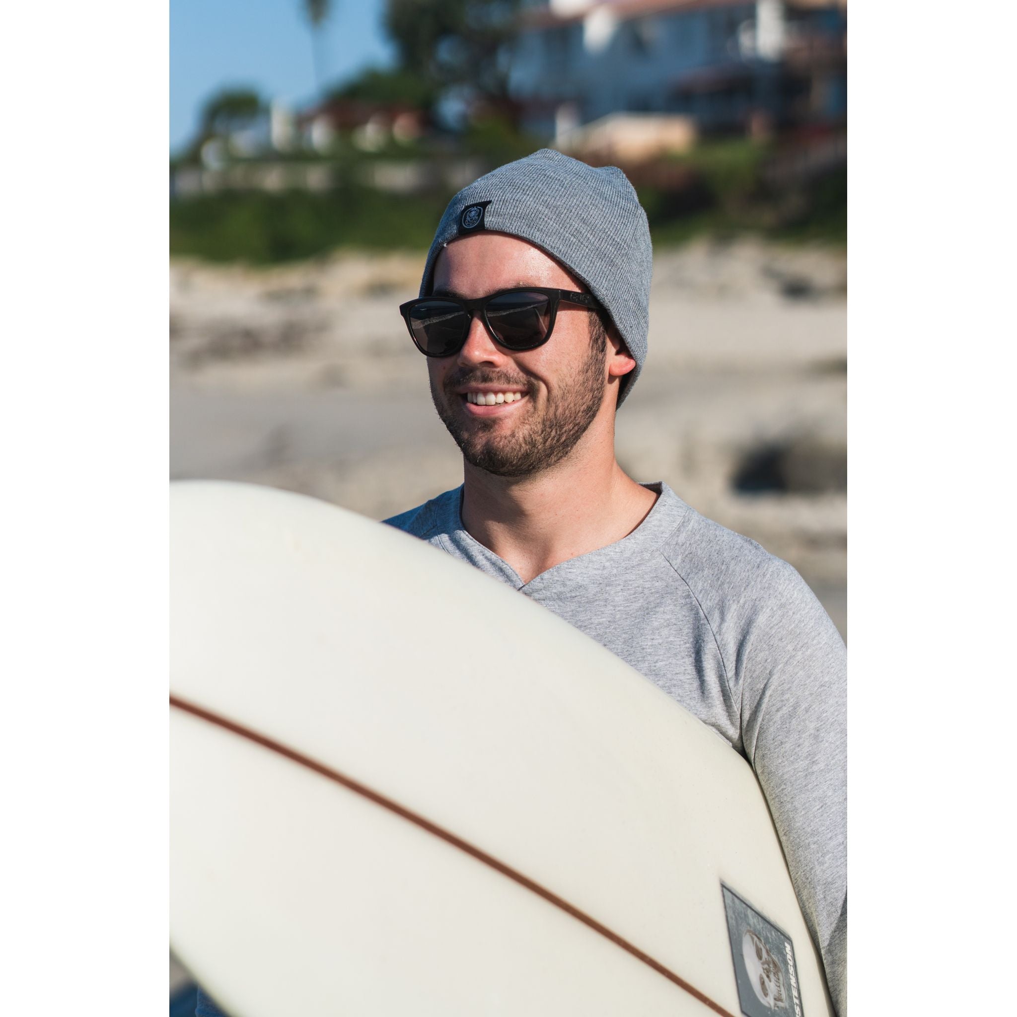 Sport Beanie - man wearing gray beanie while smiling and carrying a surfboard on the beach