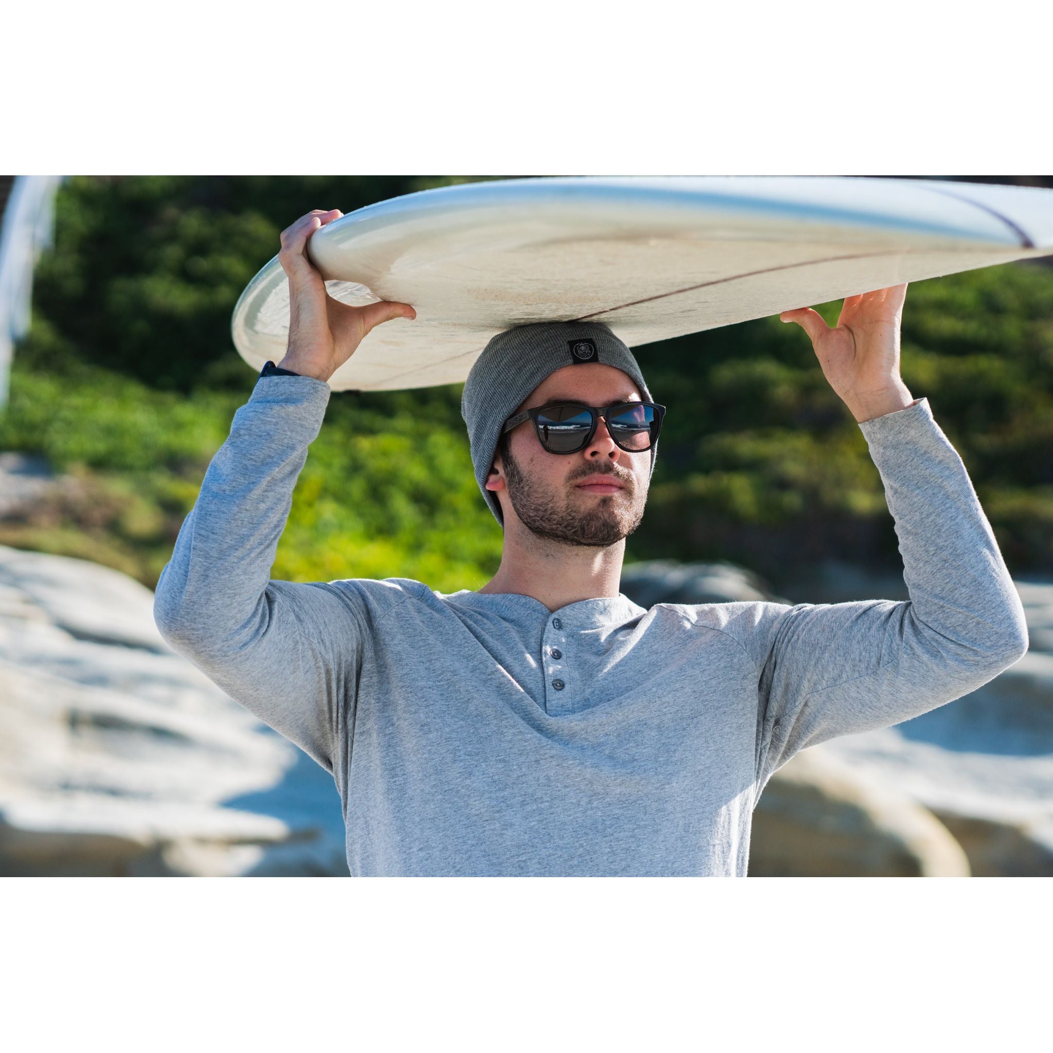 Sport Beanie - man wearing gray beanie while carrying surf board over his head