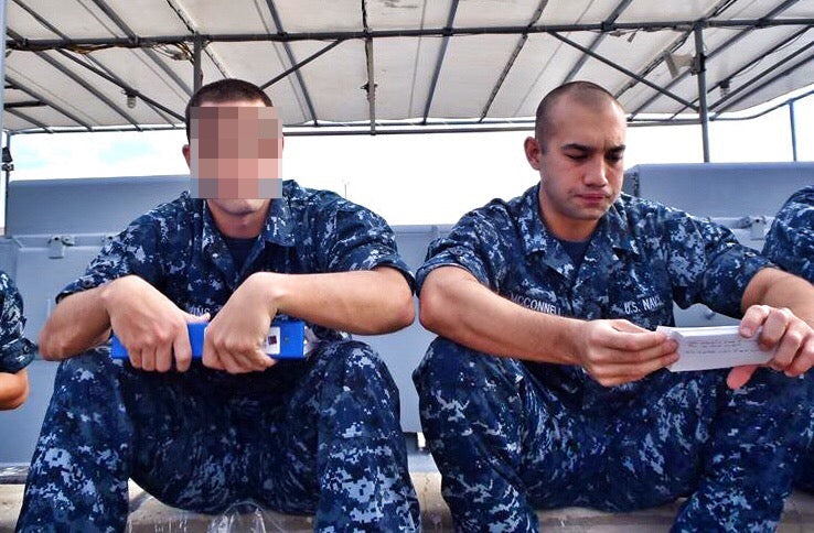 Two men in camouflage sitting next to each other holding paperwork
