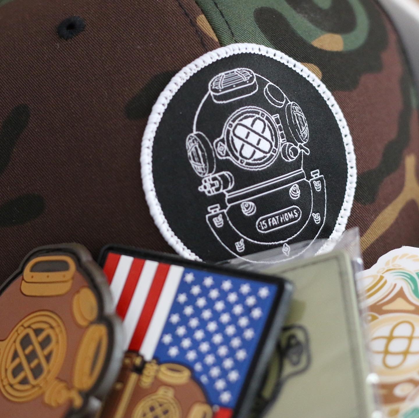 15 Fathoms diver helmet logo on a camo hat with various patches lined up below