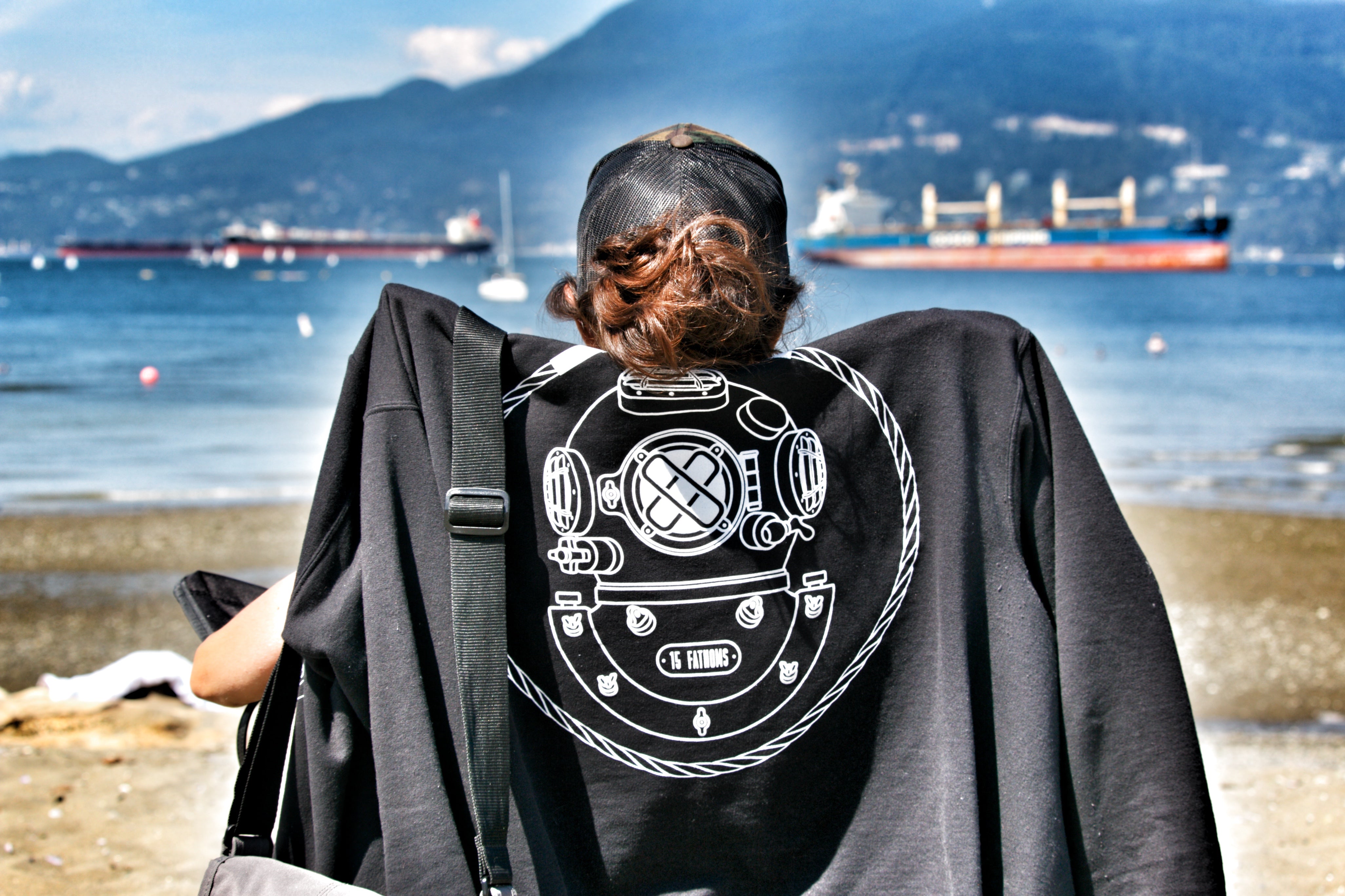 Woman on the beach sitting on a chair with a 15 Fathoms hoodie draped over the back