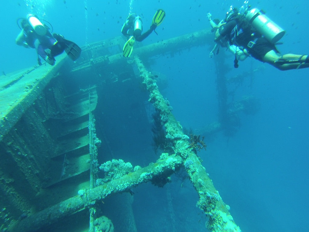 Three scuba divers exploring a sunken shipwreck underwater